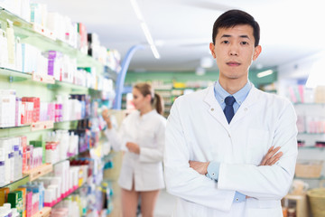 Portrait of chinese man pharmacist who is standing on his work place in apothecary.