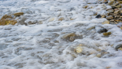 pebble stones on the sea beach, the rolling waves of the sea with foam