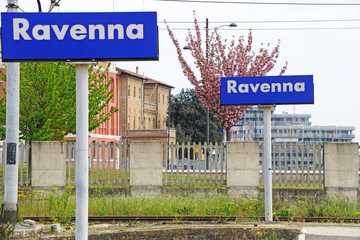 A sign with the name of the city of Ravenna, Italy. Railway station, background