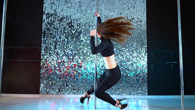 Sexy dancer in black moving in high heels shoes with pylone in night club or studio. Pole dancing. Shining background. Dance, sex, temptation concept.