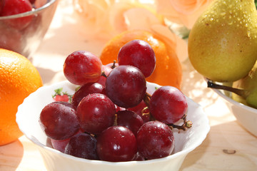 Juicy red grapes, pears and oranges on a light background with drops close-up, tasty, dietary and healthy food for a healthy lifestyle.