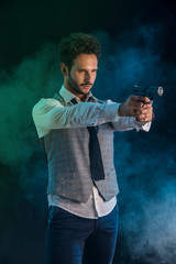 Elegant man with gun, pointing it at someone off frame, on smoky dark background