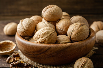 Walnuts in wooden bowl on rustic background. Selective focus.