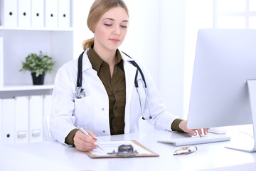 Young woman doctor at work in hospital looking at desktop pc monitor. Physician controls medication history records and exam results. Medicine and healthcare concept