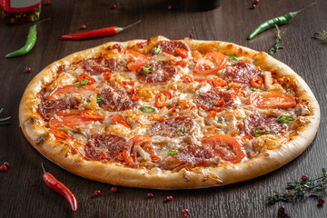 Diablo's pizza close-up on a wooden table next to peppers and condiments.