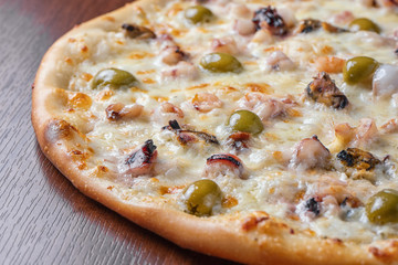 Pizza with shrimp and olives close-up on a wooden table.