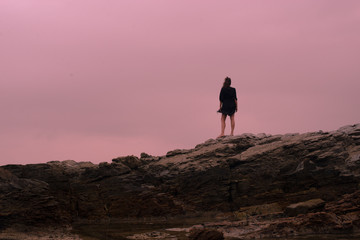 Woman standing on rocks shot from behind with dramatic skyline in background