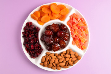 Mix of dried fruits and nuts on a white plate. Apricot, almond, raisin, dates fruit. On a lilac background. Space for text or design.