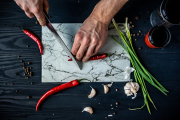 Slicing fresh red chili pepper with a knife on a cutting board. Chef cooking at a kitchen. Salsa, guacamole preparation. Mexican food.