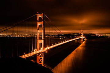 Fototapeta na wymiar The golden gate bridge in San Francisco California taken on a cool summer night. The skyline of the city glows in the distant horizon as the building lights provide a urban background to the scene