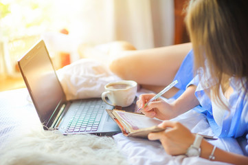 young sexy girl with morning coffee lies in bed writes e diary and works with a netbook