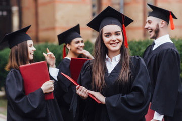 Young students dressed in black graduation gowns. Students holding diplomas,