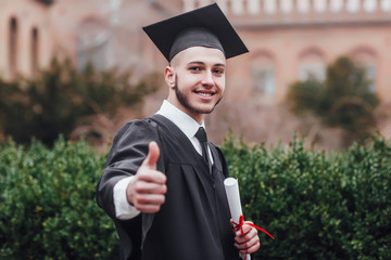 Young handsome graduated man holding degree , doing ok sign with fingers, excellent symbol!