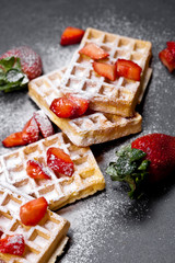 Belgium waffers with strawberries and sugar powder on black board.