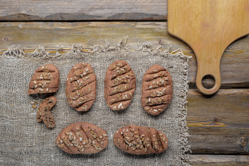 whole wheat bread with sunflower seeds and knife with cutting board and burlap on wooden background, top view 