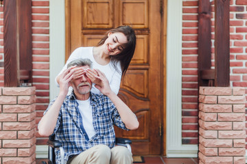 Cheerful disabled grandfather in wheelchair welcoming his happy granddaughter .