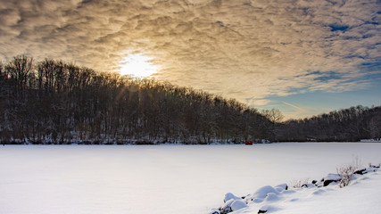 bright orange yellow sunset in clouds warms the scene of ice fishing with red hut on frozen lake at twin lakes park greensburg pa with fishermen standing on ice waiting