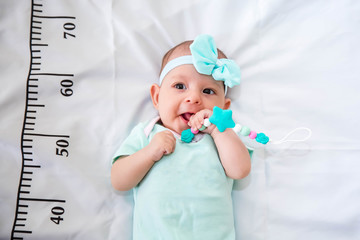 A three month baby in mint green clothes lying on a bed on which a measuring ruler for growth is...