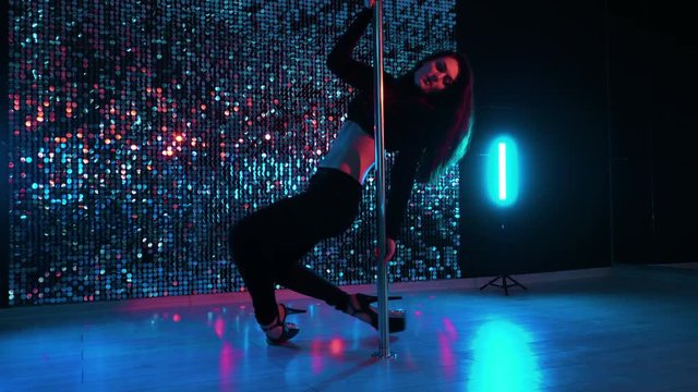 Sexy dancer in black moving in high heels shoes with pylone in night club or studio. Pole dancing. Shining background. Dance, sex, temptation concept.