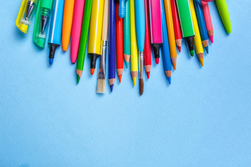 Colored pens, pencils, markers and other objects lie on a light blue background.
