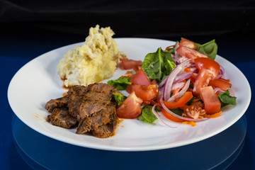 BBQ Beef Brisket on White Plate with Potatoes and Salad against Reflective BG
