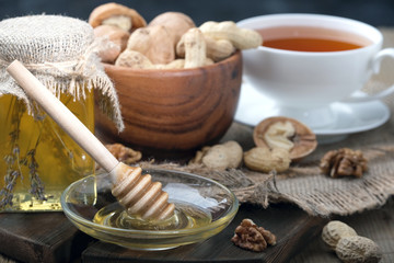 Honey jar, honey platter with spoon and peanuts, walnuts in a wooden cup, on a wooden table.