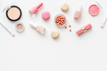 Make-up artist desk with powder, nail polish, decorative cosmetics and macaroon cookies white background top view mokeup