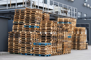 Stacks of colorful rough wooden pallets at warehouse in industrial yard. Wooden pallets for industrial transportation by truck. Cargo and shipping concept.