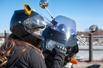 Fototapeta na wymiar Biker girl in helmet with mask clenches fist while sitting in front of plastic front cowl with headlight of her motorcycle