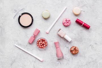 Make-up artist desk with powder, nail polish, decorative cosmetics and macaroon cookies on stone background top view