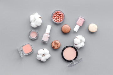 Make-up artist desk with powder, nail polish, decorative cosmetics and macaroon cookies on gray...