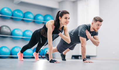 Fototapeta na wymiar Young couple doing push-ups from the floor on one hand together on the background of fitness balls. Sporty male and female in sportswear training in the sports club.