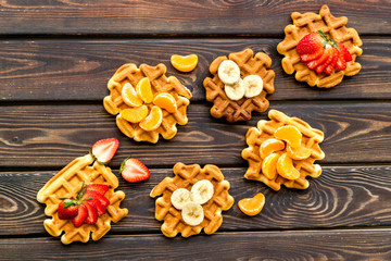 Traditional belgian waffles with fruit topings on wooden background top view