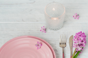 Pink rustic place setting with purple hyacinth flower, candles and linen napkin on white wooden background