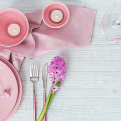 Pink rustic table setting with purple hyacinth flower, candles and linen napkin on white wooden table
