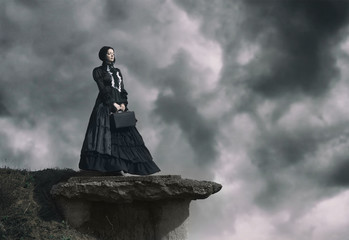 Outdoors portrait of a victorian lady in black standing on the cliff.