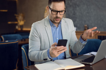 Young worried businessman text messaging on smart phone in a cafe