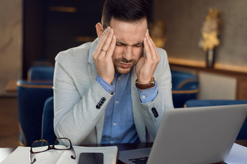 Mid adult businessman having headache while working on laptop in a cafe