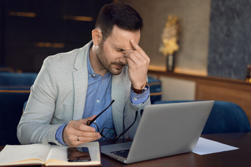 Mid adult businessman having headache while working on laptop in a cafe