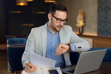 Shot of a pensive businessman checking the time while working on reports in a cafe