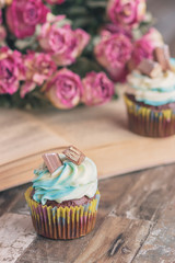 Handmade chocolate muffins with decorations. Book and a bouquet of roses, blurred background