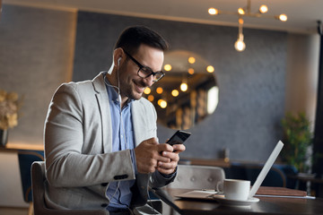 Mid adult businessman surfing the internet on his smart phone in a cafe