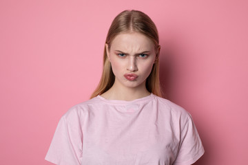 Fototapeta premium Portrait of cute young blonde girl looking angry at camera, having doubtful and indecisive face expression