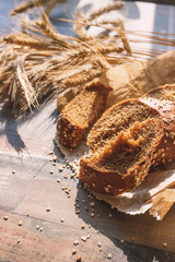 Handmade bread with bran and ears of wheat, wooden background