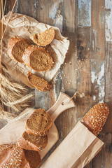 Handmade bread with bran and ears of wheat, wooden background