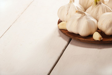 Garlic Cloves and Bulb in vintage wooden plate on white wooden table.