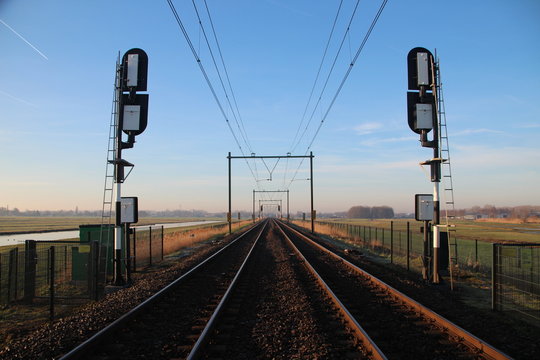 Railroad double track in Moordrecht during sunrise with signals in the low polder heading from Rotterdam to Gouda