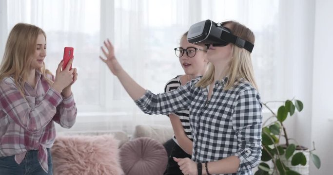 Girl using mobile phone to record video of friend playing game with VR