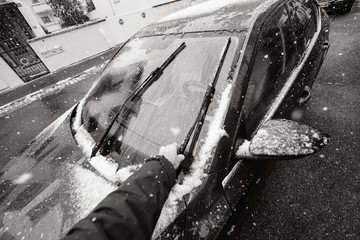 POV personal perspective of man cleaning car windshield wipers from the snow on a cold winter day before new ride black and white