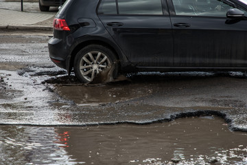 Vehicle hitting pothole in city street splashing muddy water.